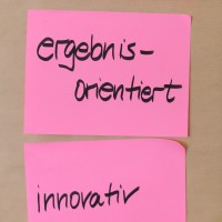 Photo von zwei pinken Post-Its auf denen ergebnisorientiert und innovativ mit schwarzem Filzer geschrieben ist.