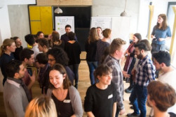 Foto von vielen Menschen in einem Raum die sich immer zu zweit gegenüberstehen (Gruppenarbeit)