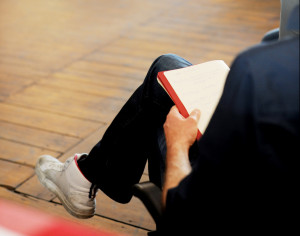 Foto auf dem man einen Körper von einer Person sieht. Die Person sitzt mit verschrenkten Beinen und hat ein Buch auf dem Schoß