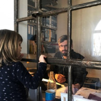 Foto mit einem Mann der arbeitet und am Fenster steht ein Kind und guckt Ihn an