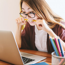 Foto mit einer Frau die vor einem Laptop sitzt und auf einen Stift beißt