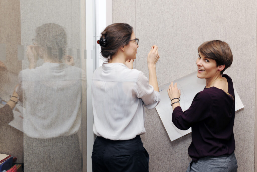 Photo von zwei denkmodell-Trainerinnen, die einen Workshop vorbereiten, indem sie ein Plakat an eine Wand hängen.